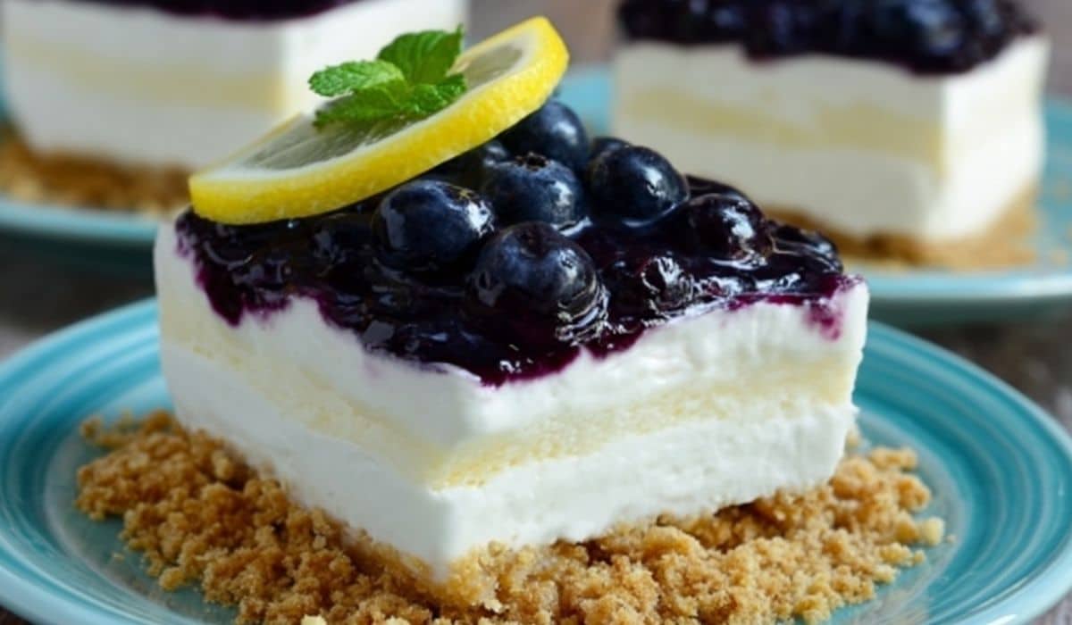 No Bake Lemon Blueberry Dessert with fresh blueberries, lemon slice, and graham cracker crust on a blue plate.