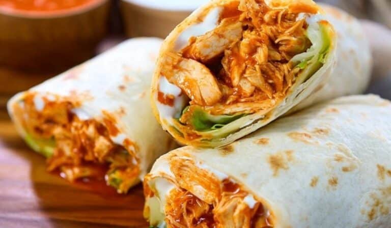 Buffalo Chicken Wraps cut in halves with ranch dressing on a wooden board