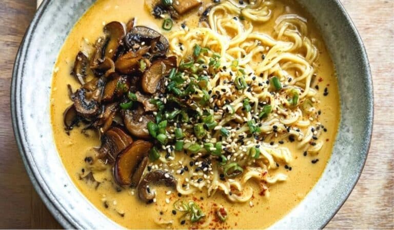 Bowl of spicy coconut curry ramen with sautéed mushrooms and scallions