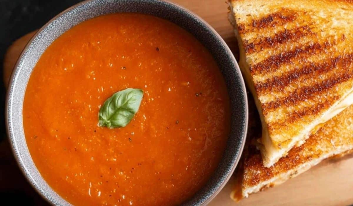 Tomato soup and grilled cheese served in a black bowl with fresh basil