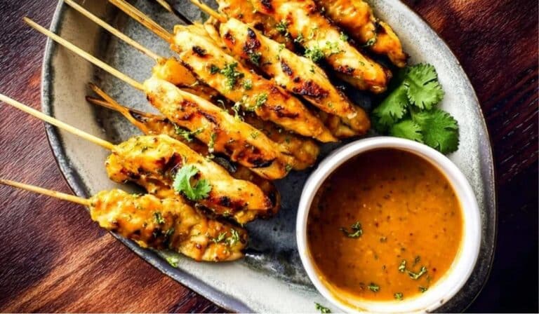 Chicken Satay with Peanut Sauce served on skewers with creamy peanut dip and fresh herbs