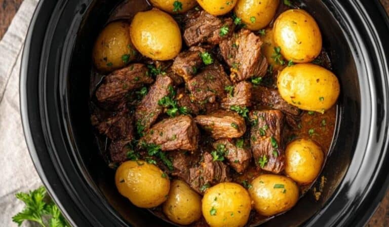 Crockpot Steak and Potatoes slow-cooked in a black crockpot with golden baby potatoes and herbs