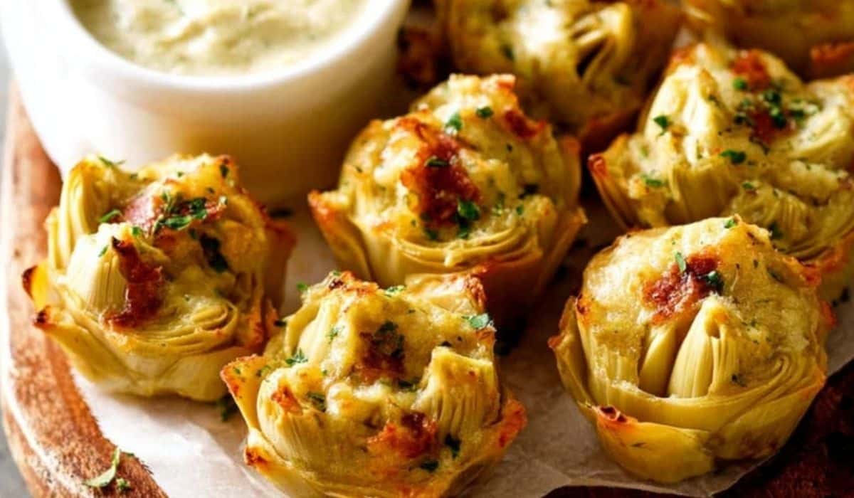 Crispy baked artichoke bites with creamy dipping sauce on wooden tray