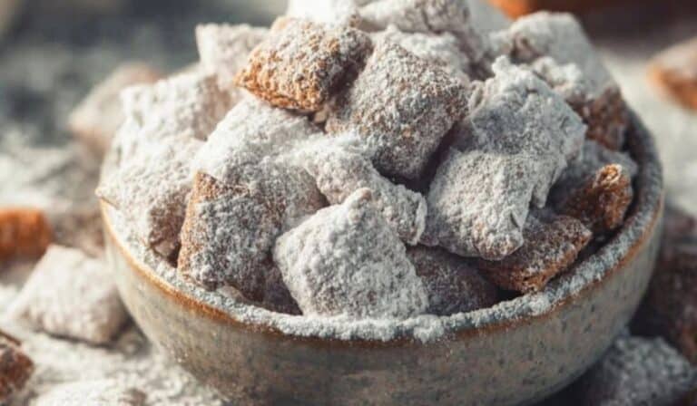 Midwestern Puppy Chow coated in powdered sugar in a rustic ceramic bowl