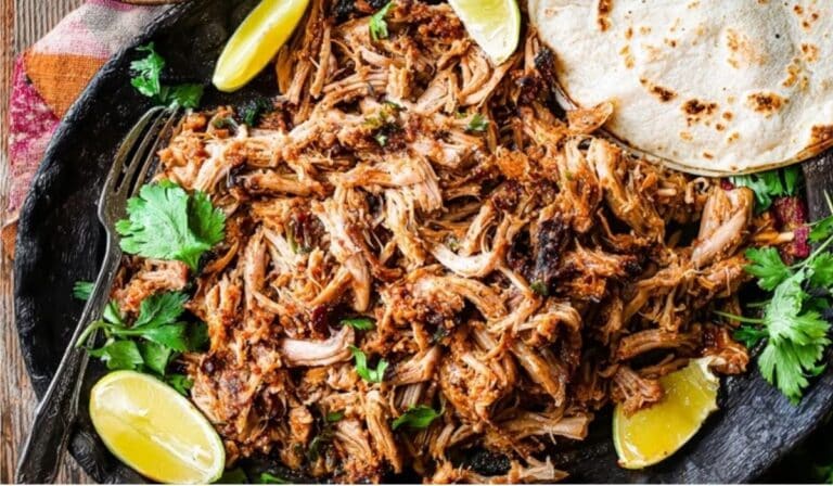 Slow Cooker Chipotle Pork Carnitas served in a skillet with lime and tortillas