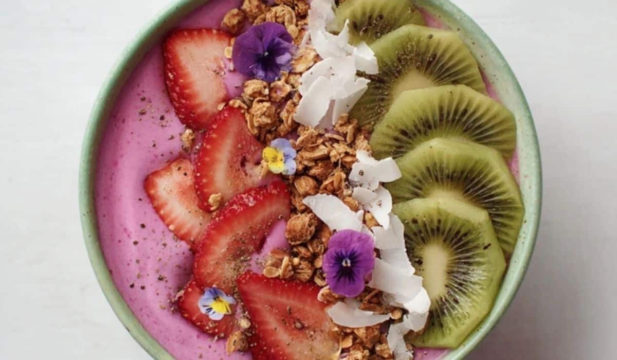 Aesthetic smoothie bowl spring edition with pink and green swirls topped with fruit, granola, and flowers.