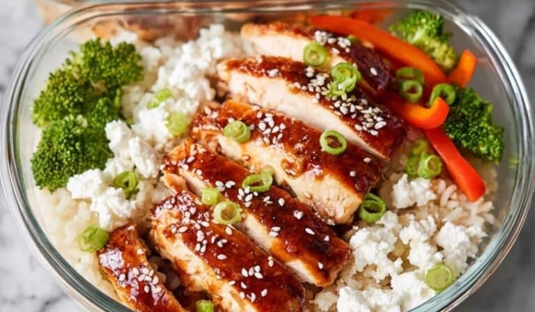 Chicken and rice meal prep bowls in glass containers with veggies on marble.